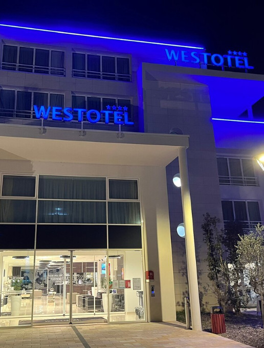Entrée de l'hôtel Westotel Tours de nuit, avec une enseigne bleue illuminée et une façade moderne en verre